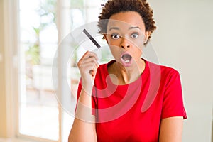 Young african american woman holding credit card scared in shock with a surprise face, afraid and excited with fear expression