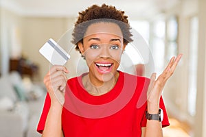 Young african american woman holding credit card very happy and excited, winner expression celebrating victory screaming with big