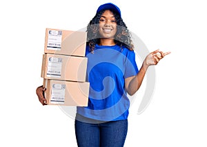 Young african american woman holding delivery package smiling happy pointing with hand and finger to the side