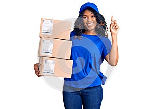 Young african american woman holding delivery package surprised with an idea or question pointing finger with happy face, number