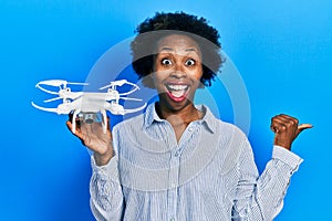 Young african american woman holding drone pointing thumb up to the side smiling happy with open mouth