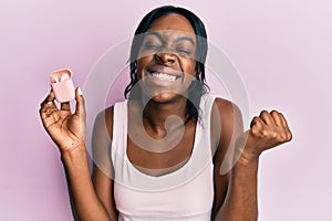 Young african american woman holding earphones screaming proud, celebrating victory and success very excited with raised arm