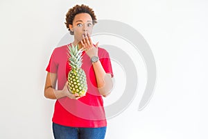 Young african american woman holding fresh healthy pineapple fruit scared in shock with a surprise face, afraid and excited with