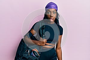 Young african american woman holding gym bag scared and amazed with open mouth for surprise, disbelief face