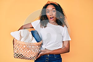 Young african american woman holding laundry basket scared and amazed with open mouth for surprise, disbelief face