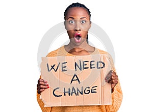 Young african american woman holding we need a change banner scared and amazed with open mouth for surprise, disbelief face