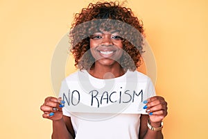 Young african american woman holding no racism banner looking positive and happy standing and smiling with a confident smile