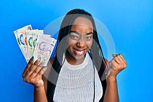 Young african american woman holding singapore dollars banknotes screaming proud, celebrating victory and success very excited