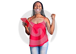 Young african american woman holding touchpad screaming proud, celebrating victory and success very excited with raised arms
