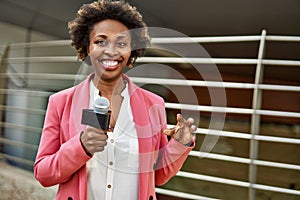 Young african american woman journalist holding reporter microphone speaking and smiling to the camera for television news