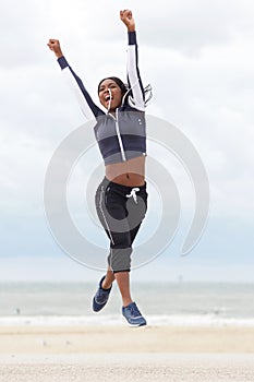 Young african american woman jumping and cheering with arms raised at the beach