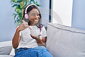 Young african american woman listening to music eating chinese food at home