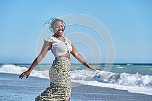young african american woman listening to music by the shore of the beach