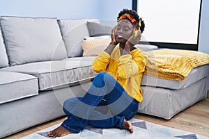 Young african american woman listening to music sitting on floor at home