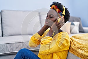 Young african american woman listening to music sitting on floor at home