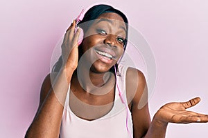 Young african american woman listening to music using headphones celebrating achievement with happy smile and winner expression