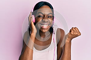 Young african american woman listening to music using headphones screaming proud, celebrating victory and success very excited