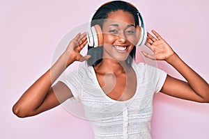 Young african american woman listening to music using headphones smiling and laughing hard out loud because funny crazy joke