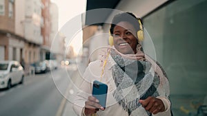 Young african american woman listening to music using smartphone at street