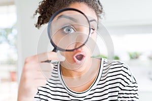 Young african american woman looking through magnifying glass scared in shock with a surprise face, afraid and excited with fear