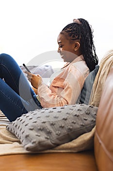 Young African American woman lounges with her phone, joy evident on her face