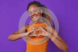 Young African American woman makes heart shape from fingers stands in studio