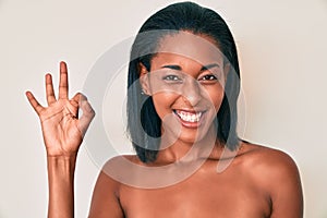 Young african american woman naked over background doing ok sign with fingers, smiling friendly gesturing excellent symbol