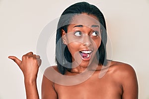 Young african american woman naked over background pointing thumb up to the side smiling happy with open mouth