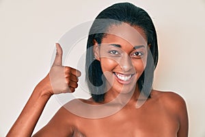 Young african american woman naked over background smiling happy and positive, thumb up doing excellent and approval sign