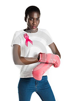 young african american woman with pink ribbon wearing boxing gloves and looking at camera