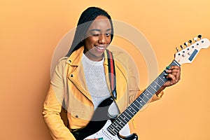Young african american woman playing electric guitar winking looking at the camera with sexy expression, cheerful and happy face
