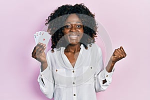 Young african american woman playing poker holding cards screaming proud, celebrating victory and success very excited with raised
