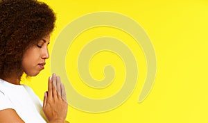 Young african american woman in prayer position wearing white t-shirt isolated on yellow background. African girl