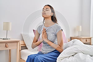 Young african american woman praying sitting on bed at bedroom