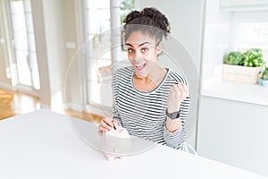 Young african american woman putting a coin inside piggy bank as invest or saving screaming proud and celebrating victory and