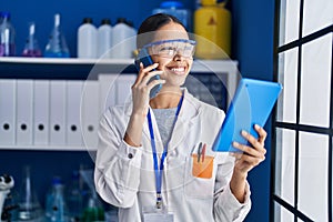 Young african american woman scientist talking on the smartphone using touchpad at laboratory