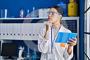 Young african american woman scientist using touchpad with doubt expression at laboratory
