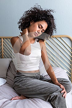 Young African American woman self massaging neck for cervical pain and discomfort after waking up in the morning.