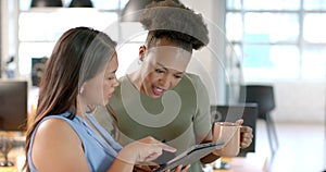 Young African American woman shares a tablet screen with a biracial woman in a business office