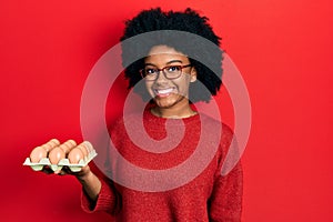 Young african american woman showing fresh white eggs looking positive and happy standing and smiling with a confident smile