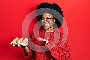 Young african american woman showing fresh white eggs smiling happy pointing with hand and finger