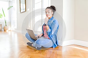 Young african american woman sitting on the floor using computer laptop serious face thinking about question, very confused idea