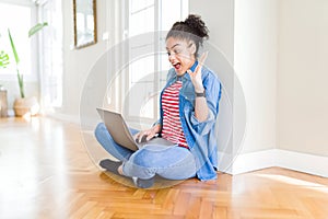 Young african american woman sitting on the floor using computer laptop very happy and excited, winner expression celebrating