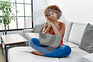 Young african american woman sitting on the sofa at home using laptop sleeping tired dreaming and posing with hands together while