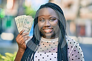 Young african american woman smiling happy holding american dollars at the city