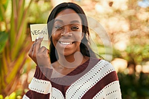 Young african american woman smiling happy holding reminder with vegan word at the park