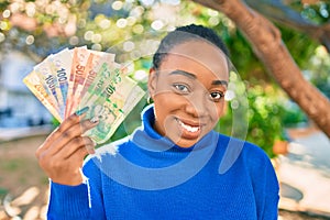 Young african american woman smiling happy holding south african rands banknotes at the park photo