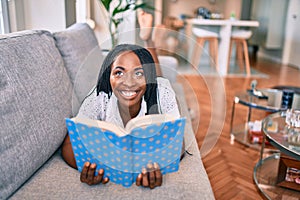 Young african american woman smiling happy laying on the sofa reading book at home