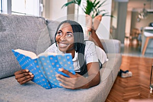 Young african american woman smiling happy laying on the sofa reading book at home