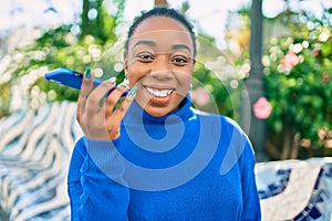 Young african american woman smiling happy sending voice message using smartphone at the park